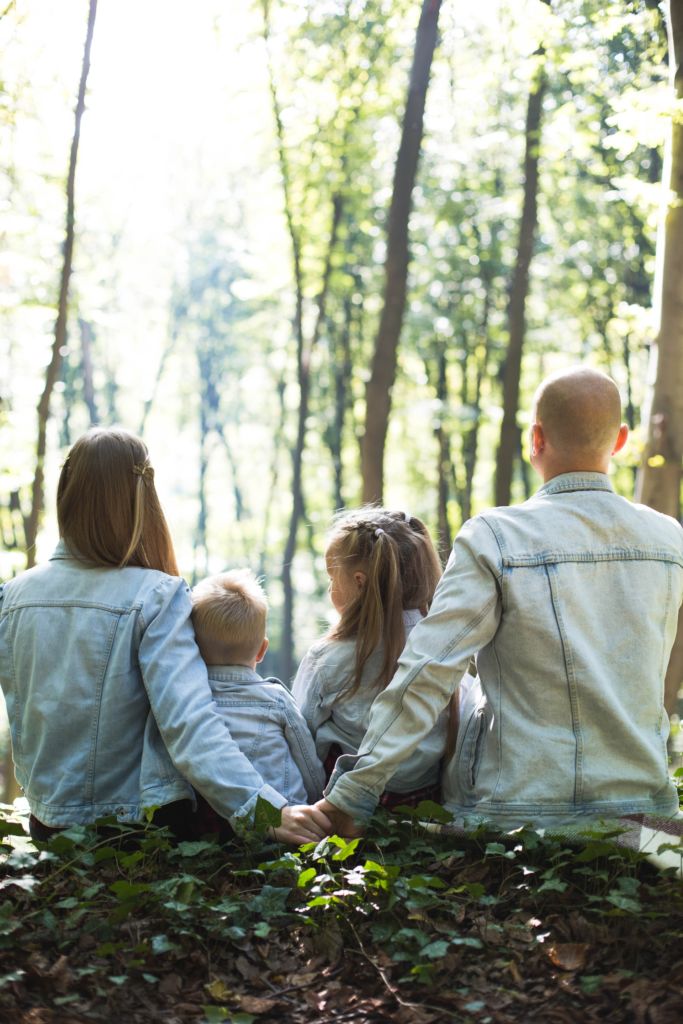 Семья из двух взрослых и двух детей сидят в лесу и смотрят на лес
